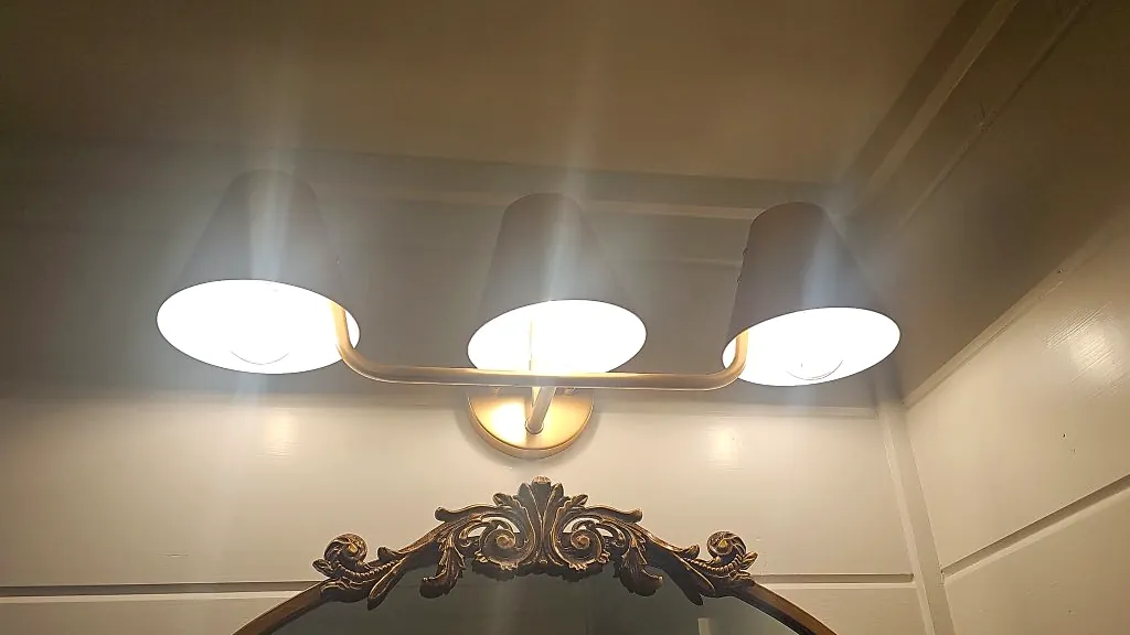Brass three-light vanity fixture above an arched mirror